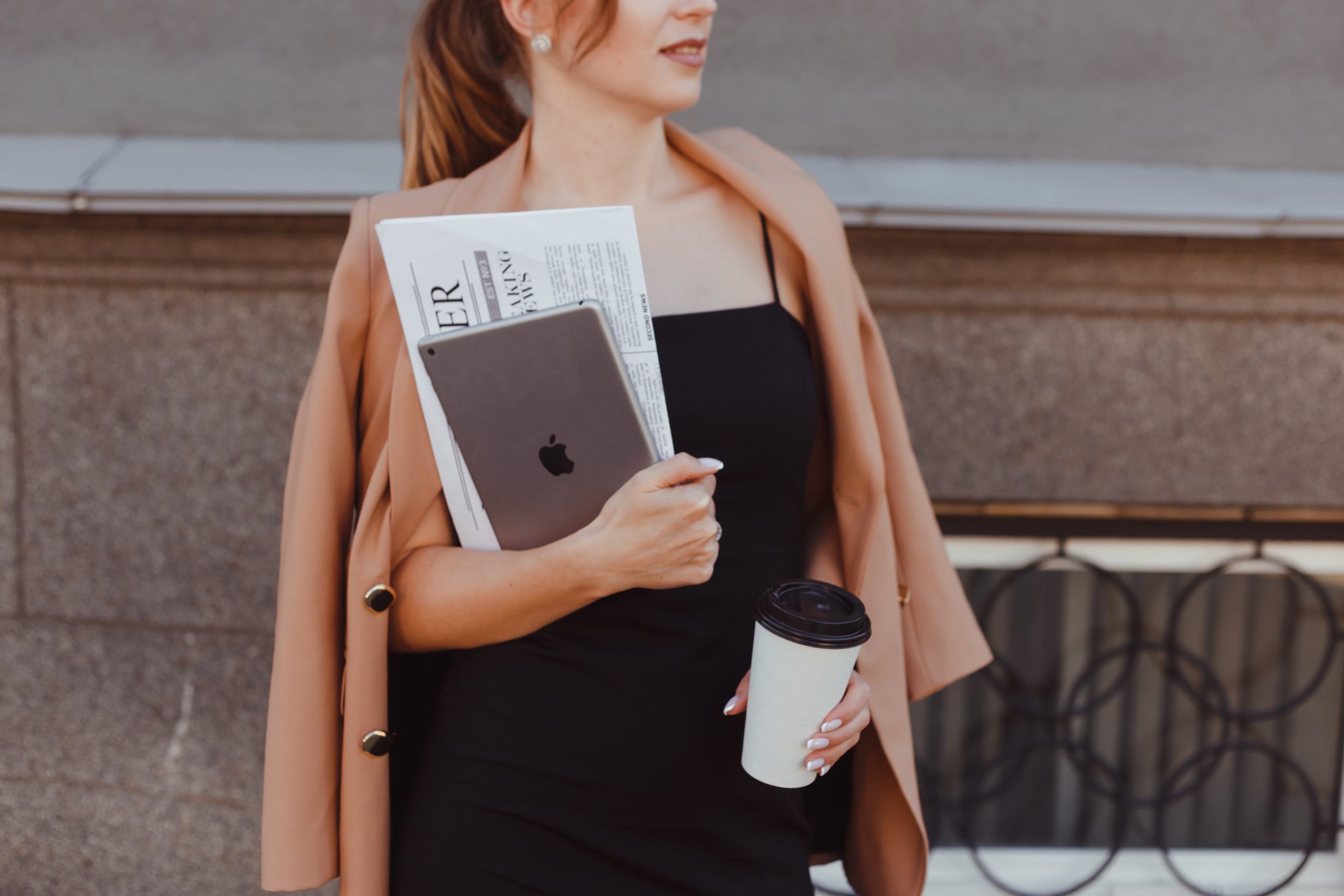 woman holding newspaper coffee and laptop outside